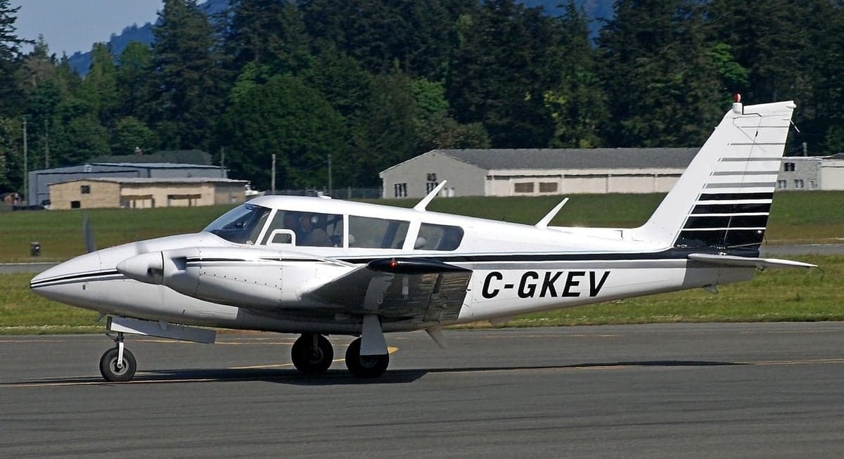 A white and black Piper PA-39 Twin Comanche taxis on the runway.