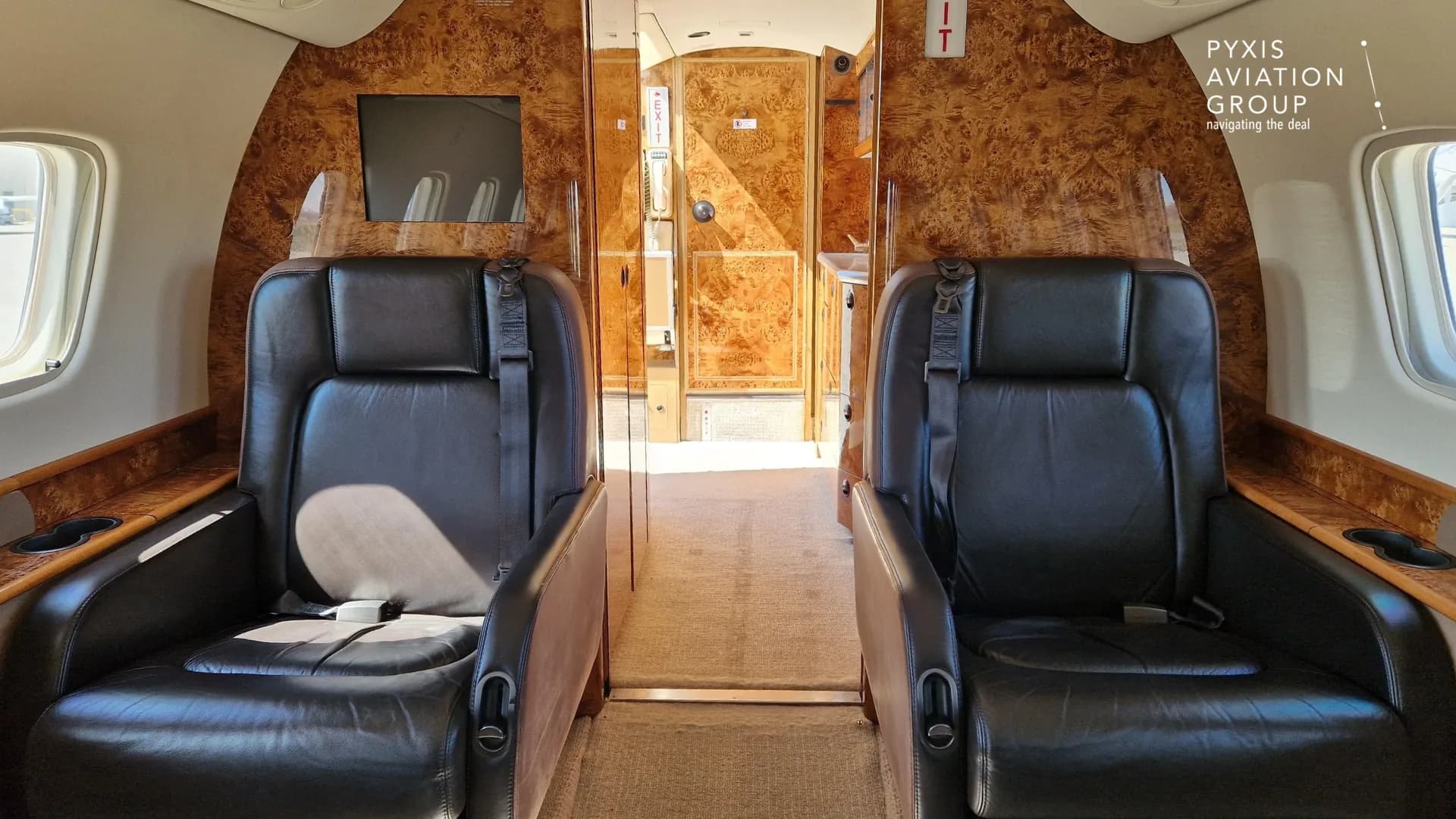 A view from inside the aircraft cabin, looking forward between two dark leather seats towards a galley or lavatory area with wood paneling.