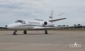 A white Cessna Citation business jet with dark stripes parked on an airport tarmac.