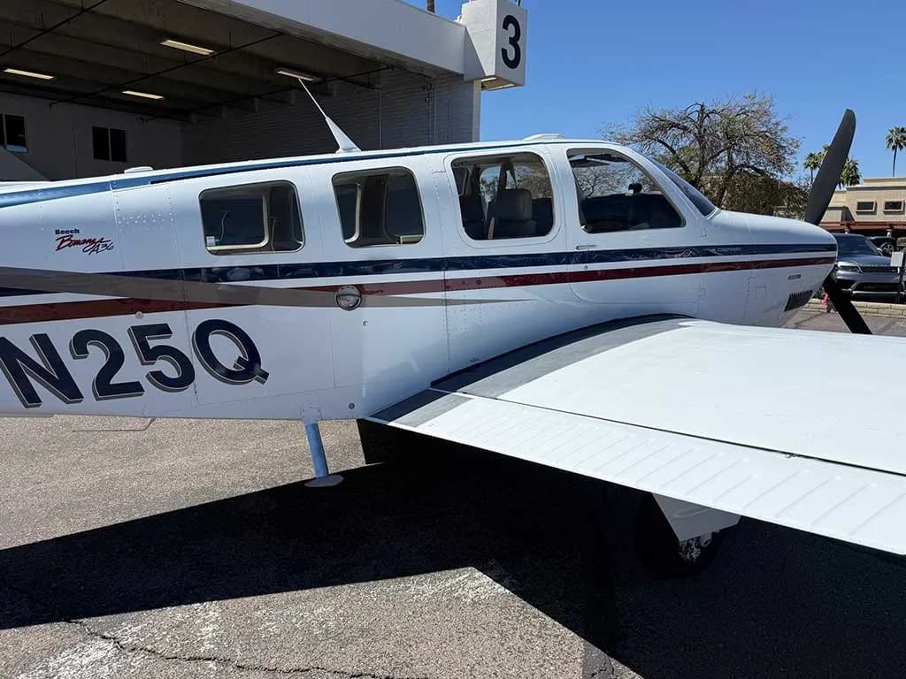 A close-up view of the mid-fuselage and right wing of the white Beechcraft Bonanza A36, registration N25Q, showing its windows and paint scheme.