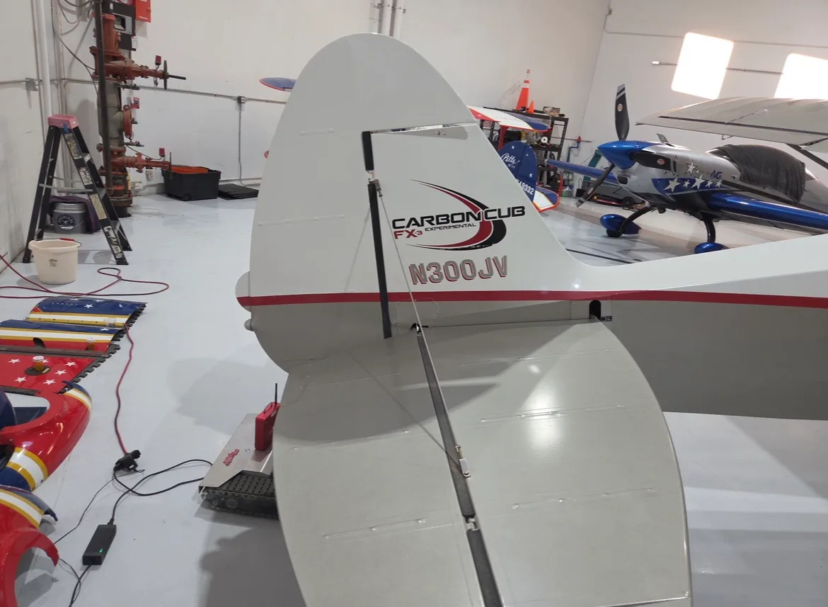 Tail view of a white and red Carbon Cub aircraft inside a hangar.