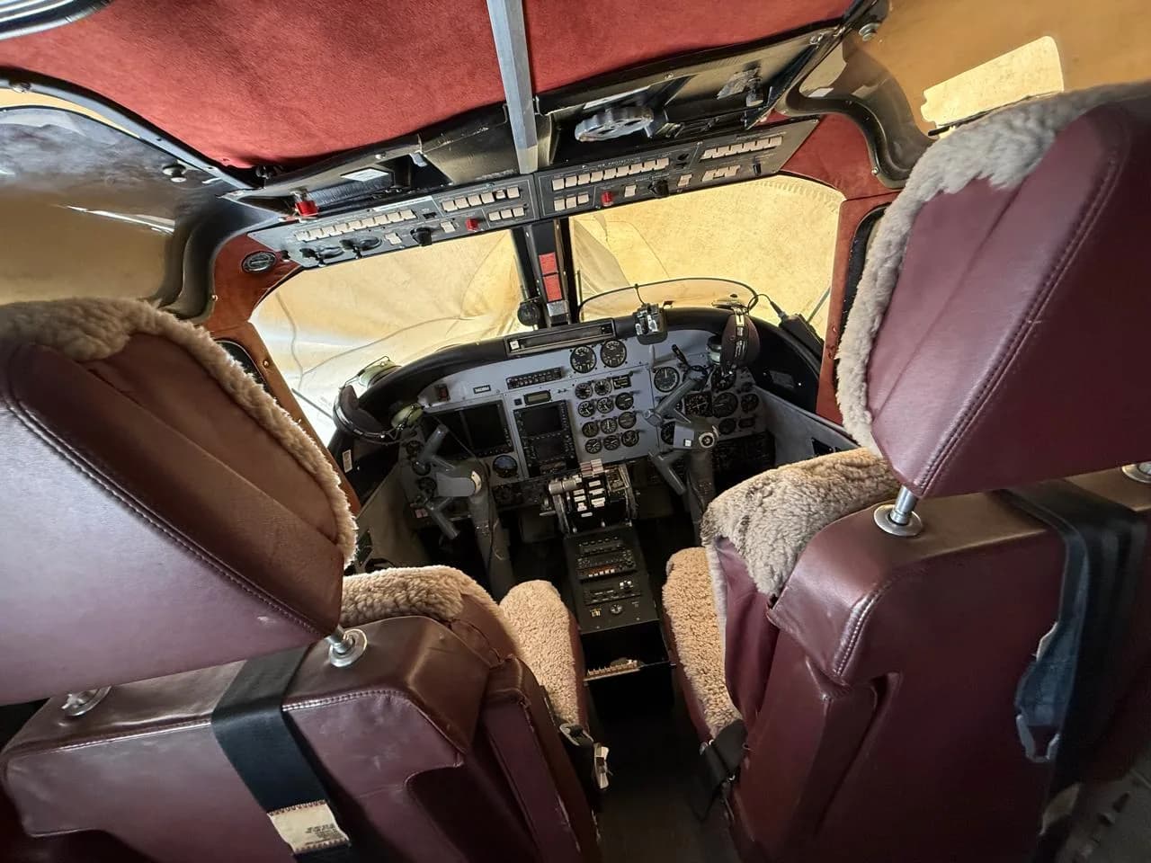 The cockpit of an aircraft features brown leather seats with sheepskin covers and a complex instrument panel.