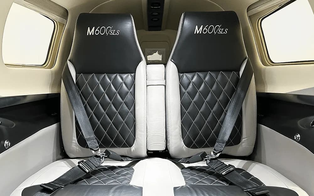 The rear passenger seats of the Piper M600/SLS cabin, upholstered in black and white quilted leather with "M600/SLS" embroidered on the headrests.