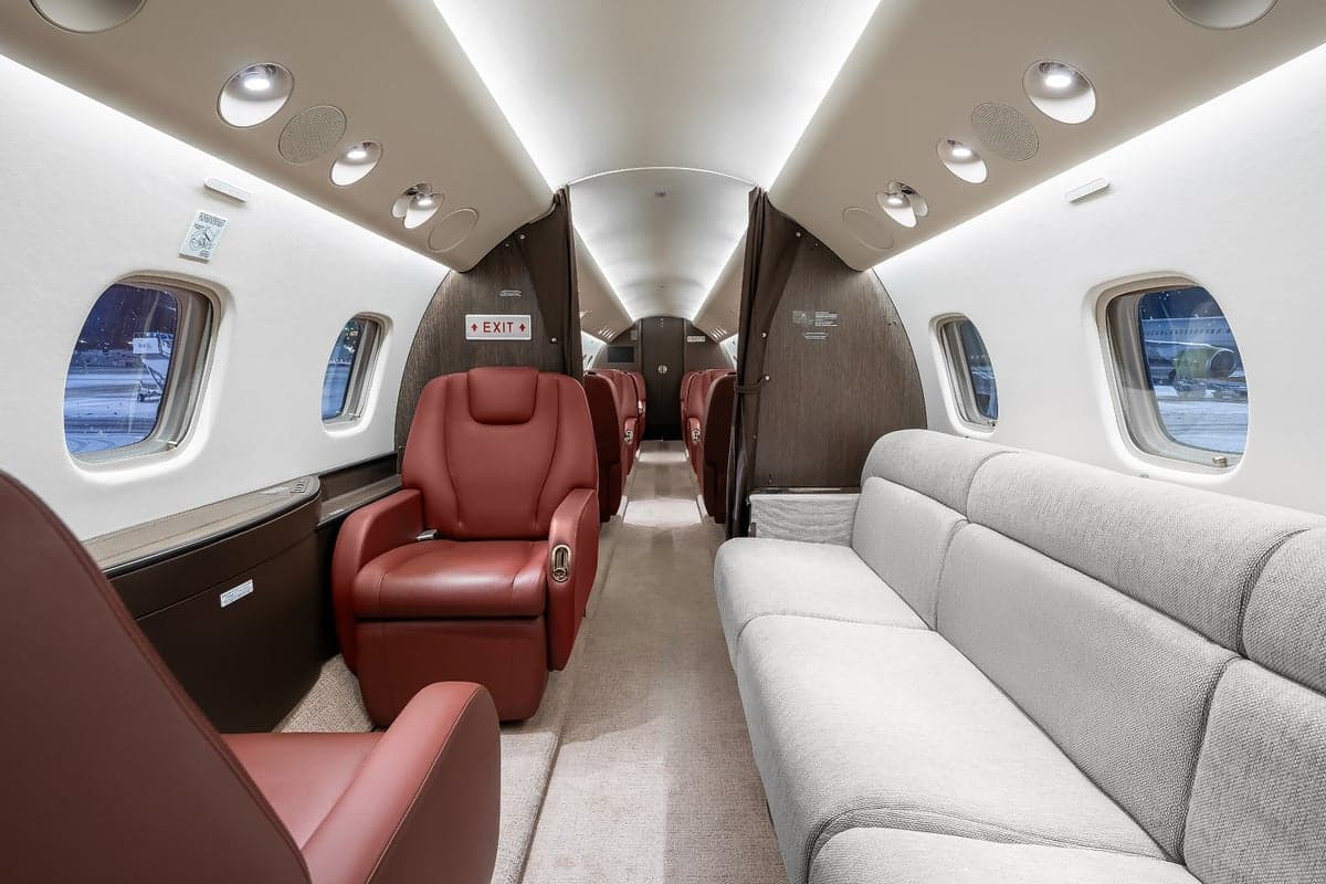 View of the aircraft interior with red leather seats, a couch, and a neutral color scheme.