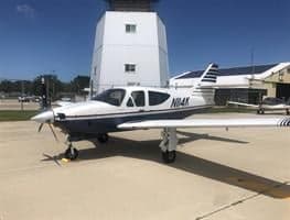 A white and blue aircraft with tail number N114K is parked in front of a control tower.