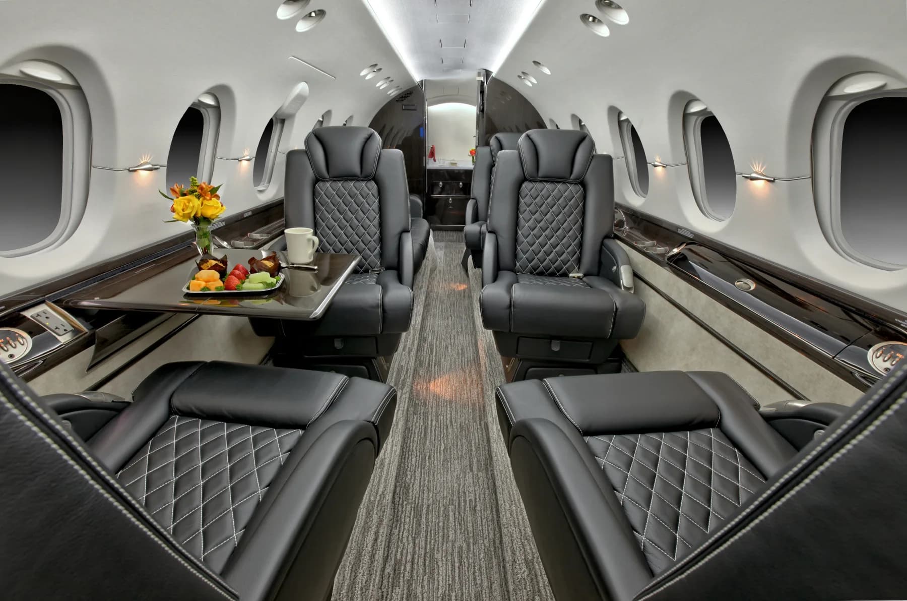 Interior view of the aircraft cabin with black leather seats, a gray carpet, and a table with refreshments.