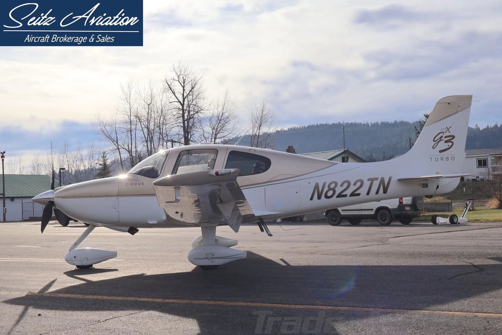 Side view of the Cirrus SR22T aircraft N822TN, parked on an asphalt ramp with a white truck and trees in the background.