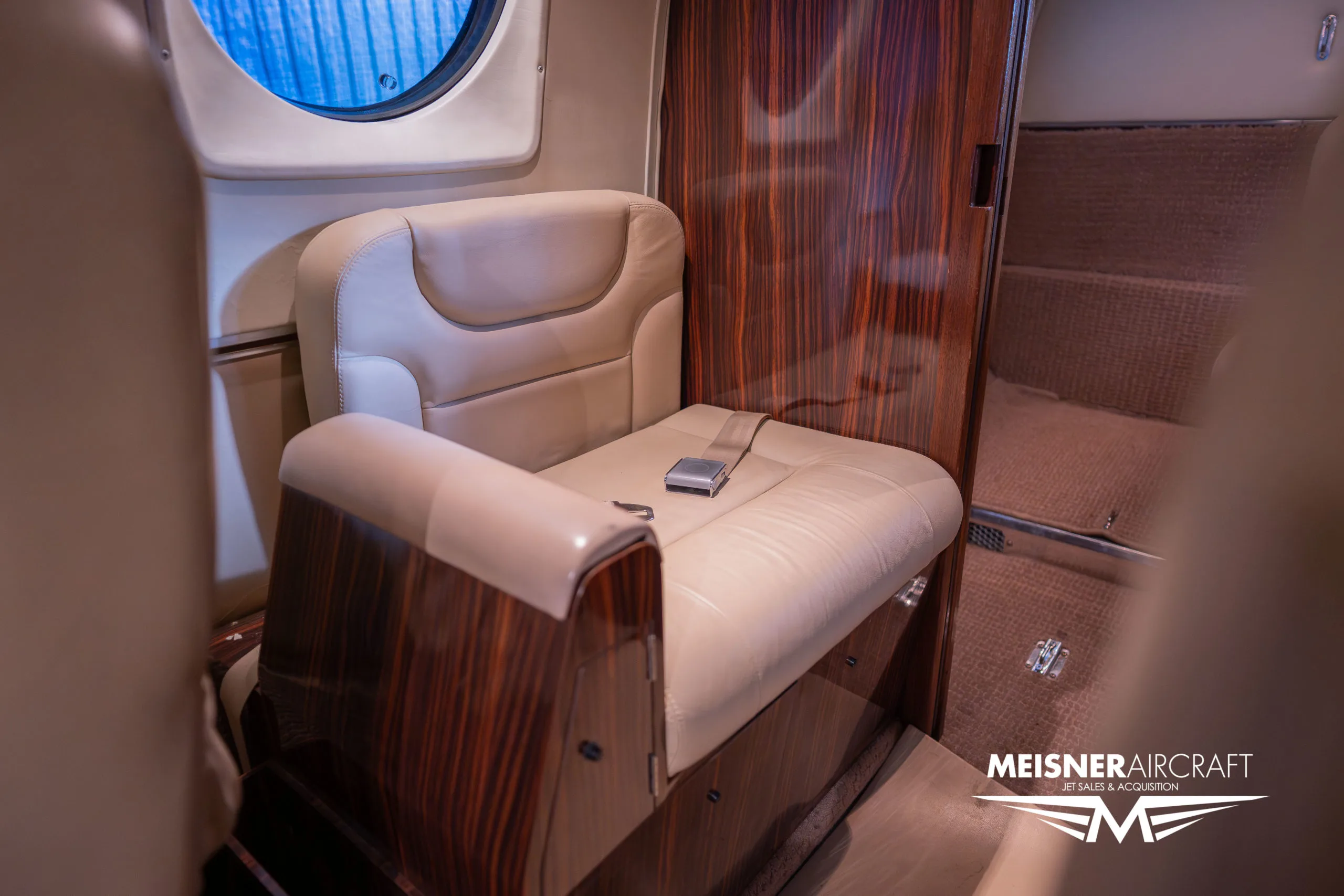 A close-up of a single beige leather seat with wood paneling in the aircraft's cabin.