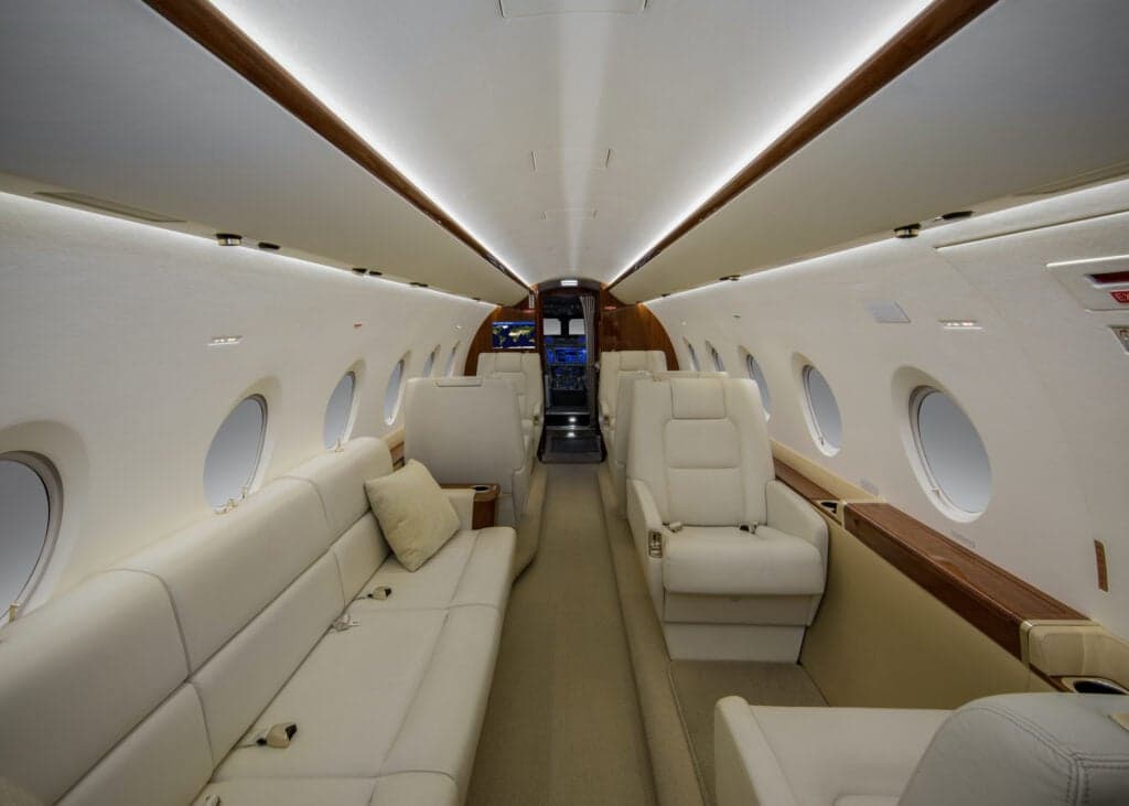Interior view of the aircraft cabin with white leather seats and tables set with food and drinks.