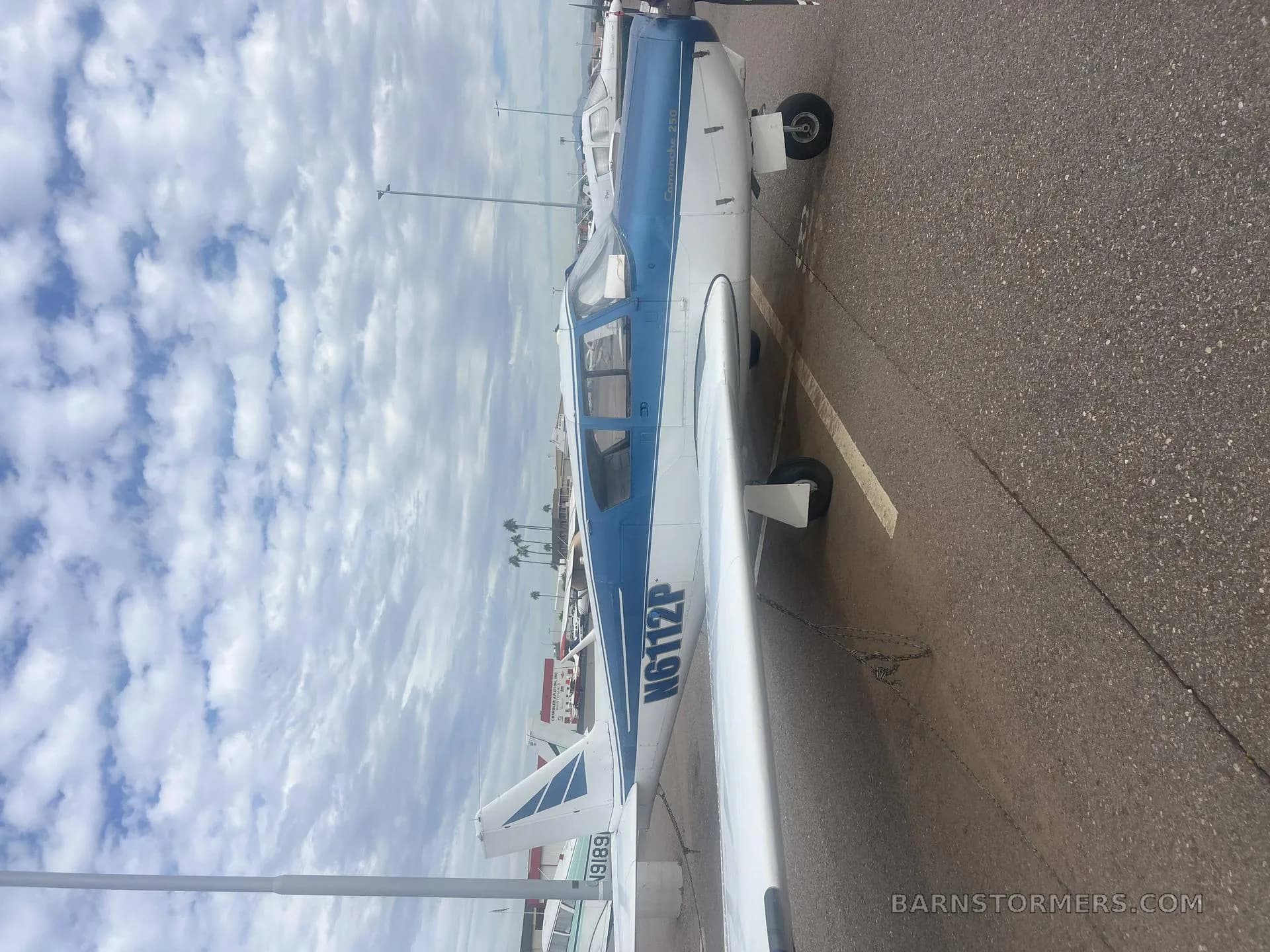 A blue and white single-engine aircraft, tail number N6112P, parked on an asphalt ramp under a cloudy sky.