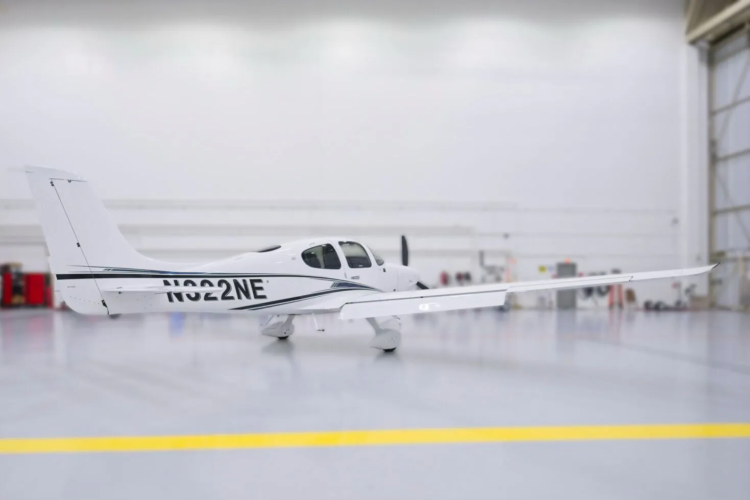 A side view of a white Cirrus SR22 aircraft with black and blue stripes, N322NE, in a hangar.