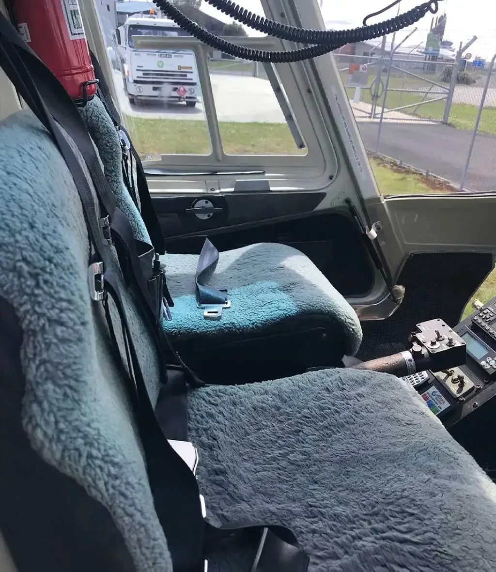 Interior view of the helicopter's front seats with light blue fuzzy covers and part of the instrument panel.