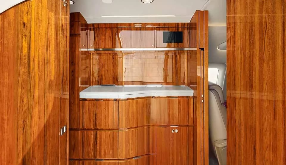 Detailed view of a private jet's galley cabinetry with polished wood and a white countertop.
