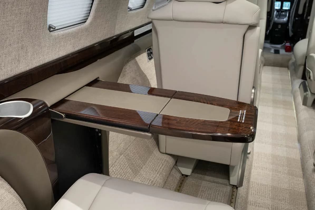 A close-up of a polished dark wood fold-out table in the private jet's cabin, next to a light-colored seat.