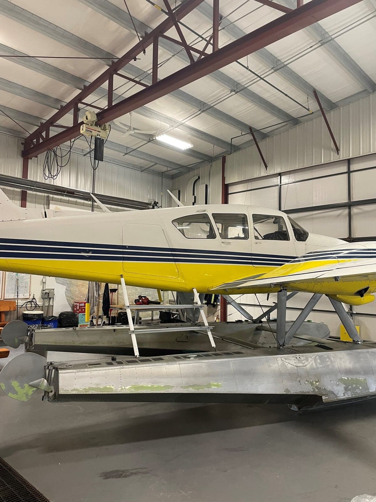 Yellow and white twin engine aircraft on floats, inside a hangar.