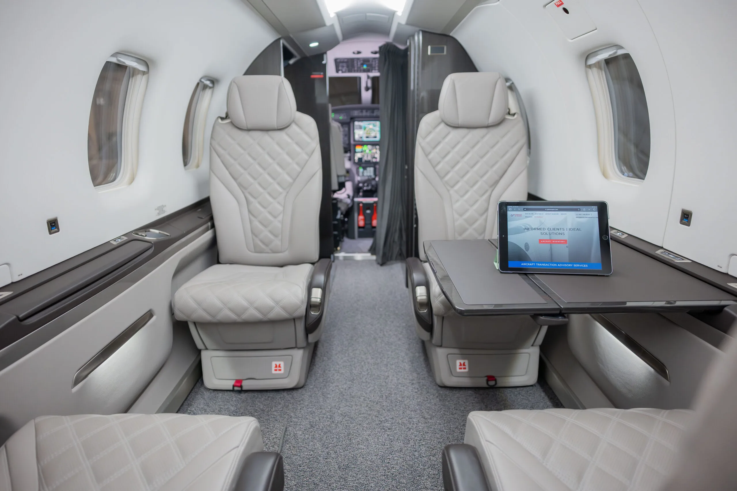 The light grey quilted leather passenger cabin of an aircraft, with a tablet displayed on a fold-out table.