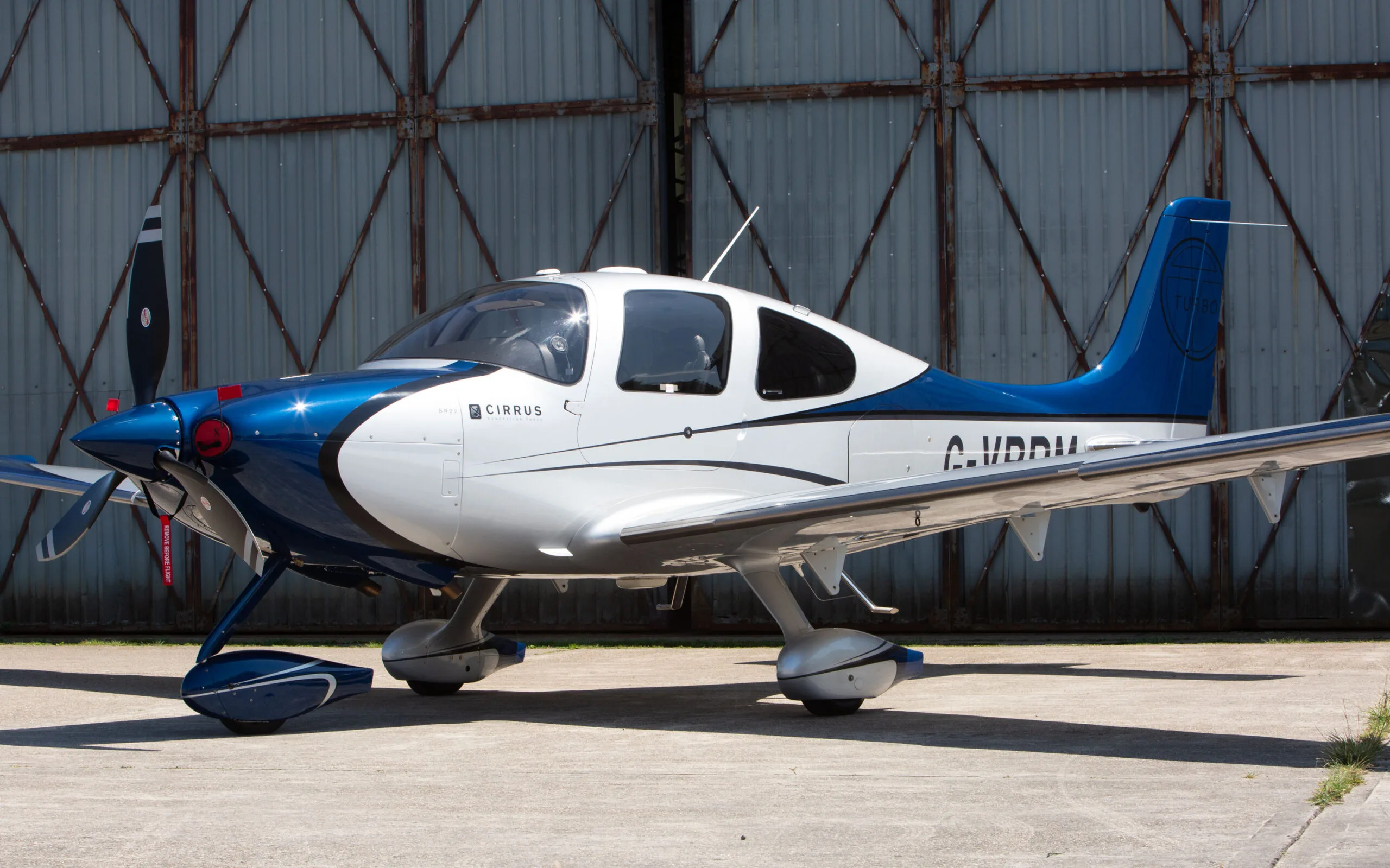 A side view of a blue and white Cirrus SR22 aircraft with registration G-VBPM, parked on an airfield apron.