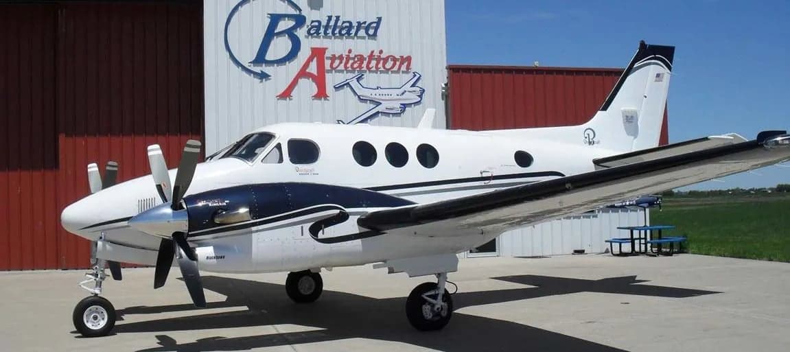 Beechcraft King Air C90B aircraft parked in front of a Ballard Aviation building.