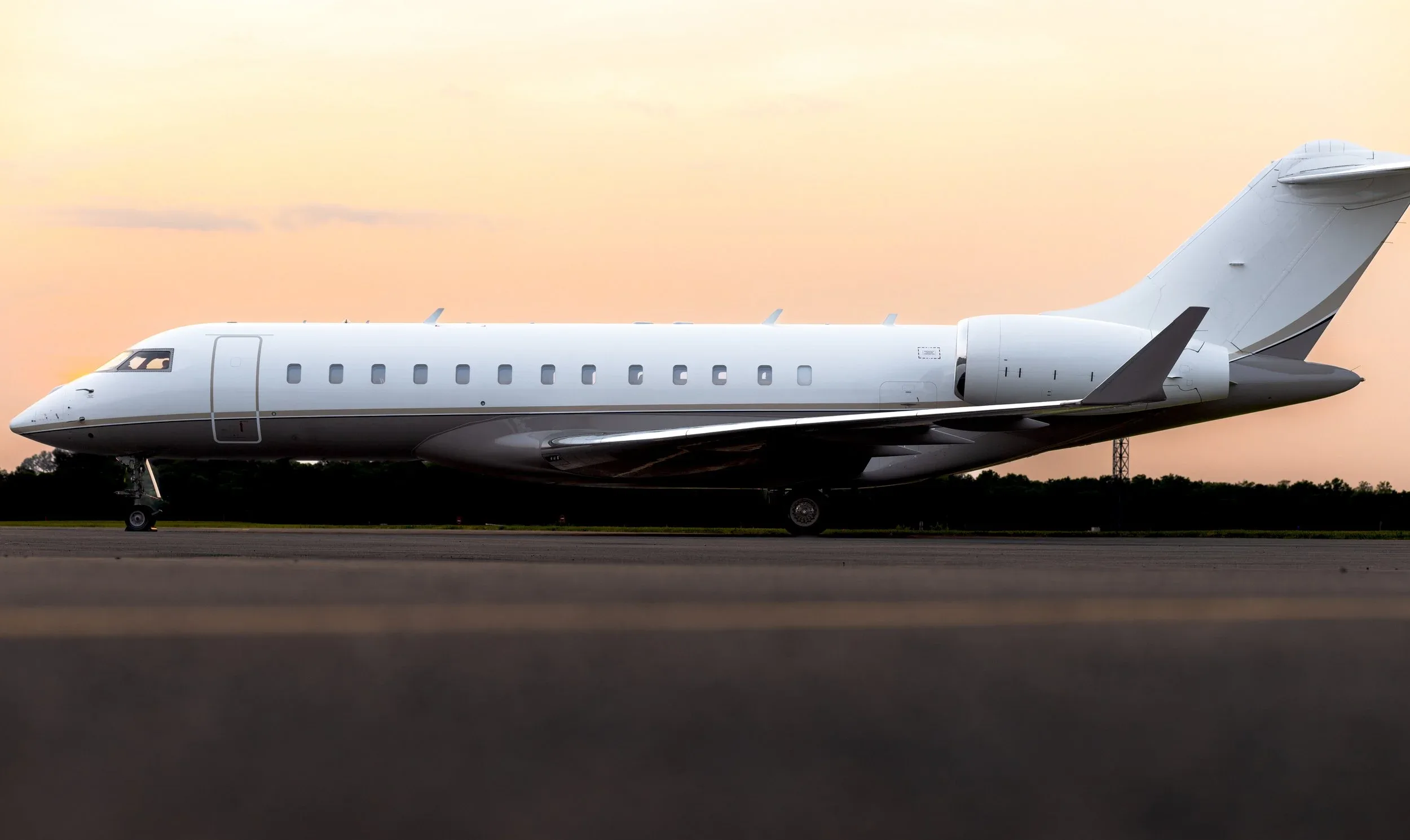 Side view of a white Bombardier Global Express aircraft on the tarmac at sunset.