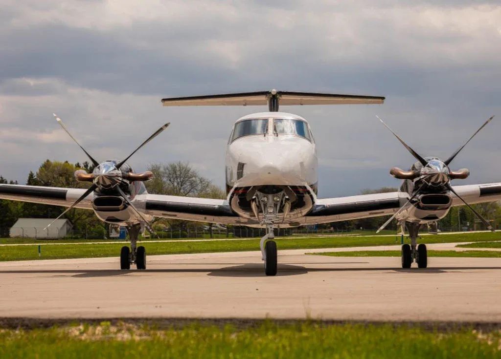 A white Beechcraft King Air 350 with black and red accents is parked on an airfield, viewed head-on.