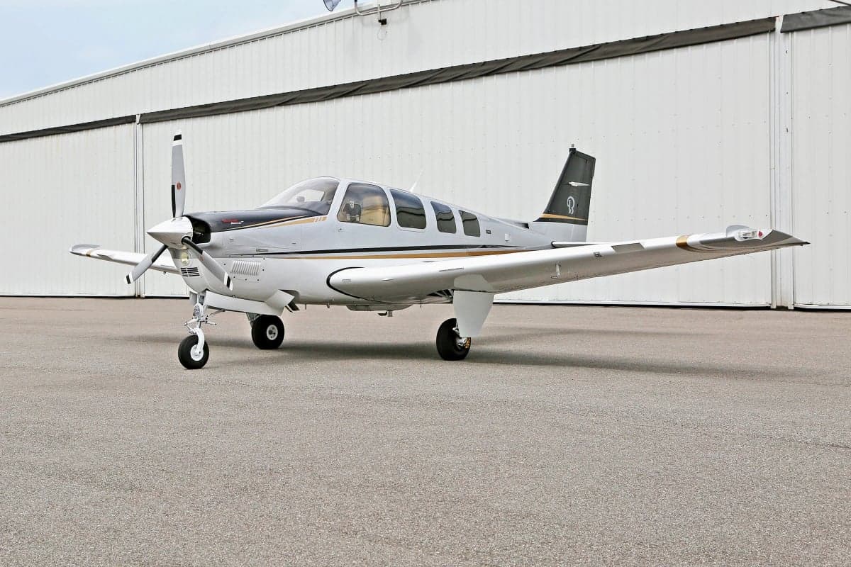 Side view of a silver and white Beechcraft Bonanza on the tarmac.