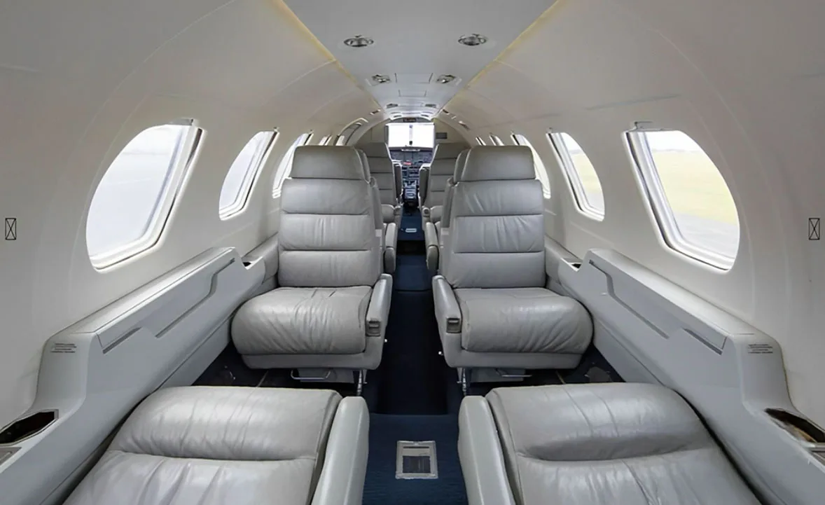 The interior cabin of a business jet with grey leather seats arranged in a club configuration.