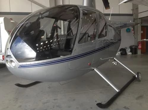 A silver helicopter with blue stripes is parked inside a hangar.