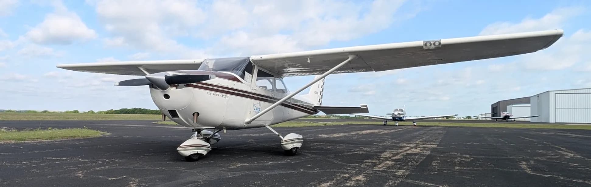 A white Cessna Skyhawk QB, registration N2740L, with a maroon stripe, parked on an airfield tarmac with hangars in the background.