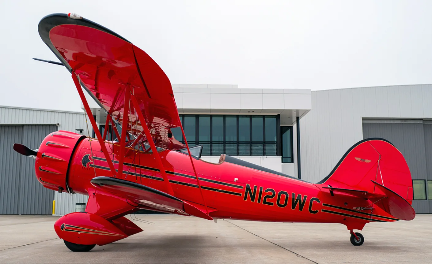 A red biplane with the tail number N120WC is parked on the tarmac.