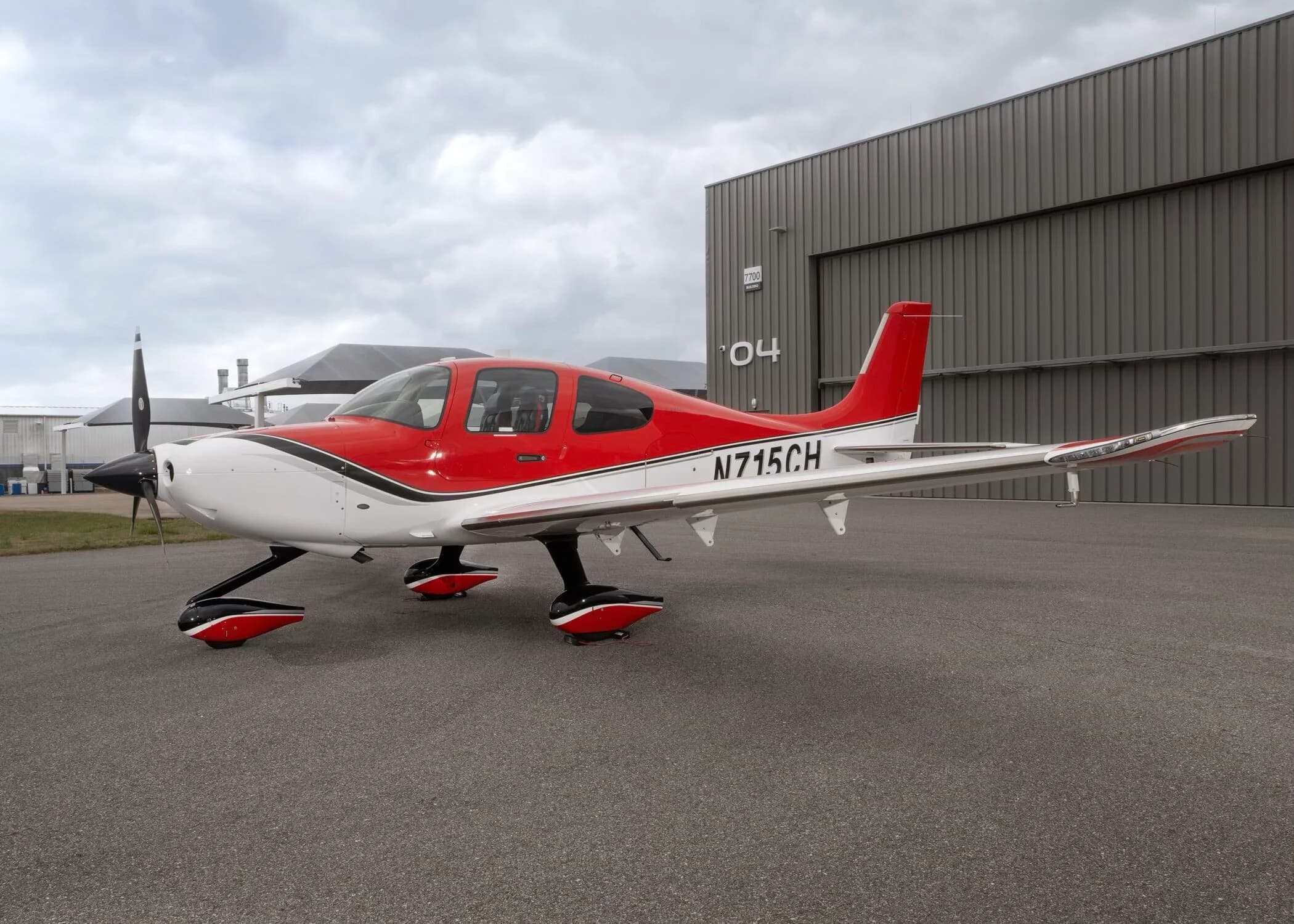 A red and white Cirrus SR22 aircraft with registration N715CH parked on an airfield next to a hangar.