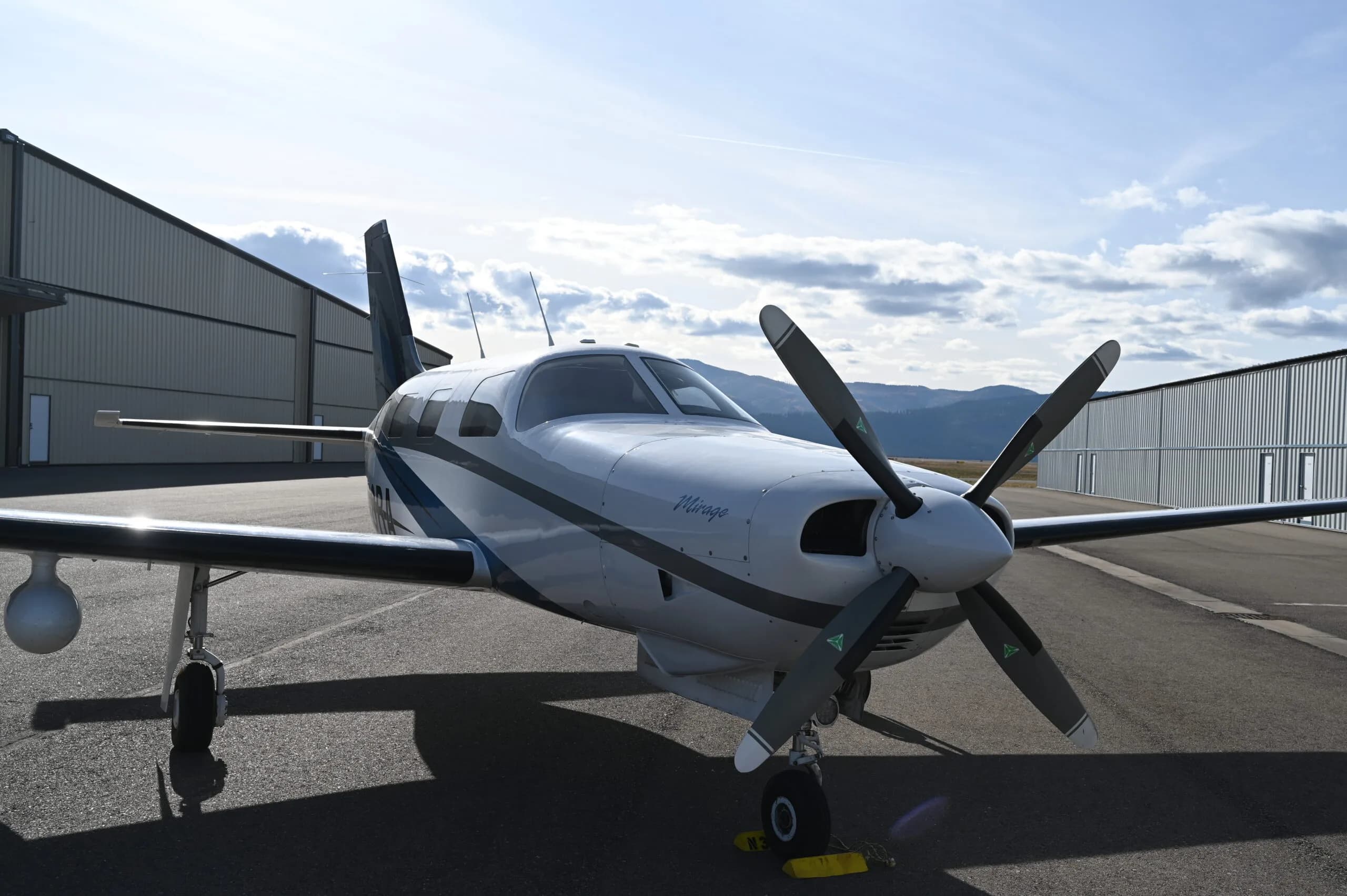 Close up front quarter view of a Piper Mirage parked on the tarmac in front of a hangar.