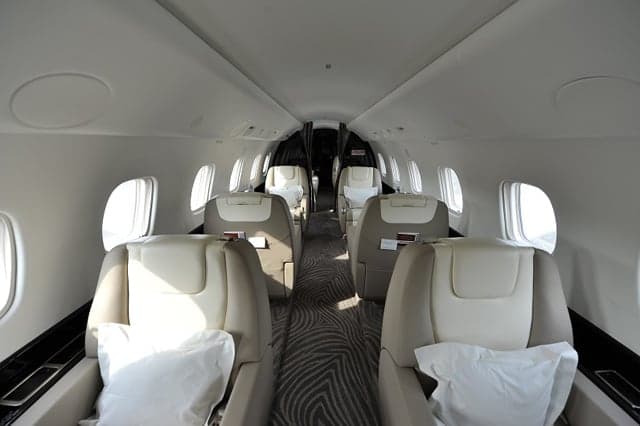 The spacious interior cabin of a private jet with multiple rows of beige and cream leather seats.