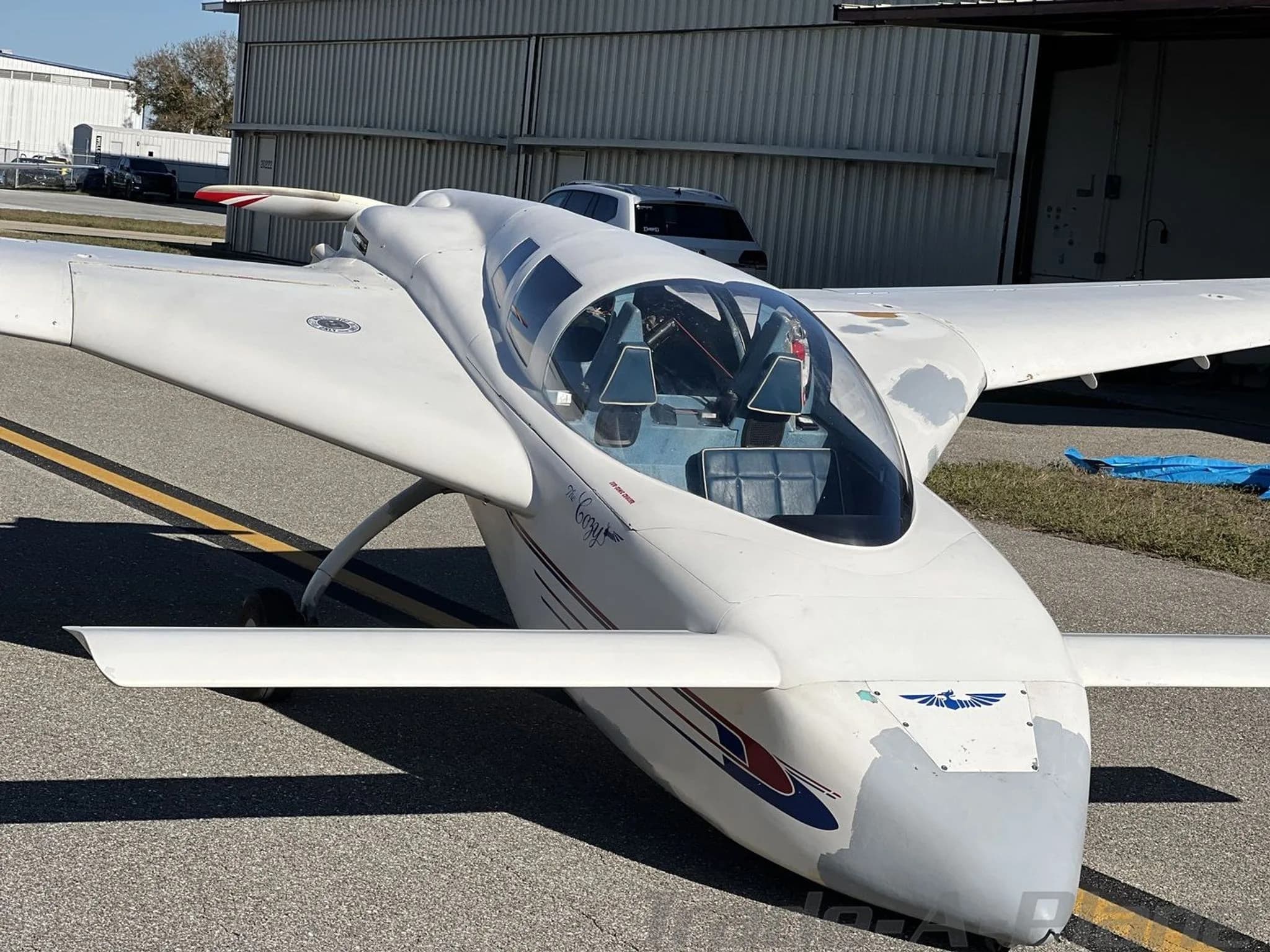 A front view of a white experimental aircraft with a clear bubble canopy and blue interior, parked on an airfield.