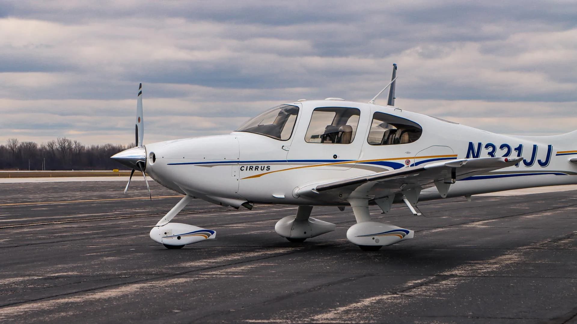A close-up side view of the white Cirrus aircraft shows its 'CIRRUS' branding and blue and gold stripe paint scheme.