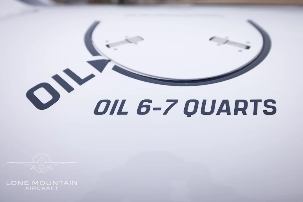 A close-up of the aircraft's white surface showing "OIL 6-7 QUARTS" text and an oil fill graphic.