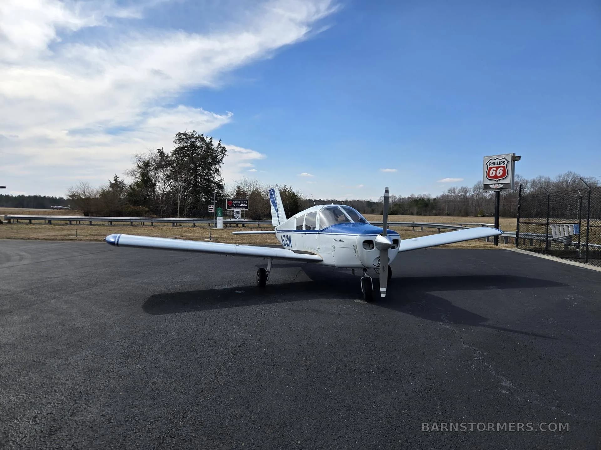 A white and blue single-engine aircraft (N5290W) parked on an asphalt ramp with a Phillips 66 sign.