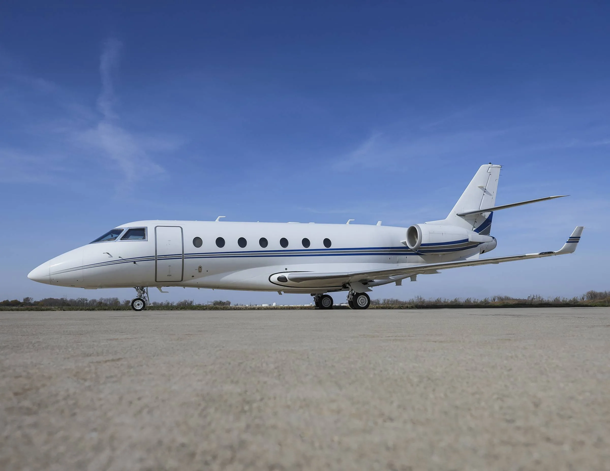 A white and blue Gulfstream jet sits on the tarmac under a blue sky.