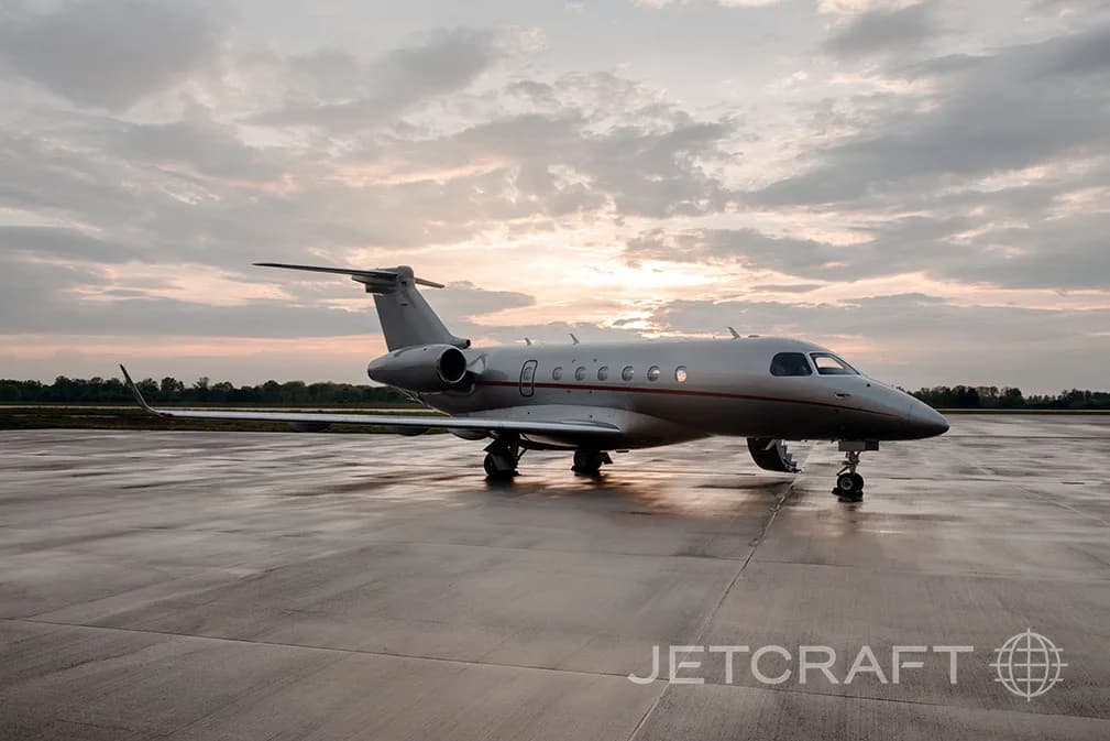 A silver jet aircraft sits on the tarmac at sunset.