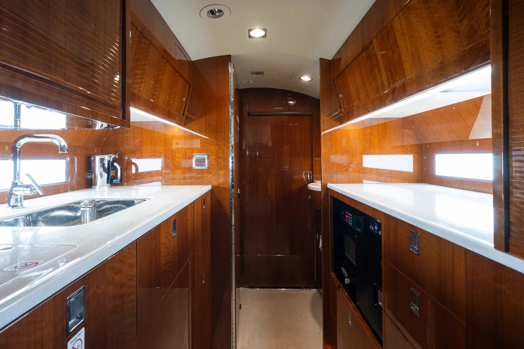 The galley area of a business jet with polished wood cabinetry and white countertops.