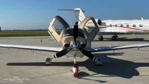 A Cirrus SR22 G3 Turbo aircraft with a white and gold paint scheme, front view with doors open.