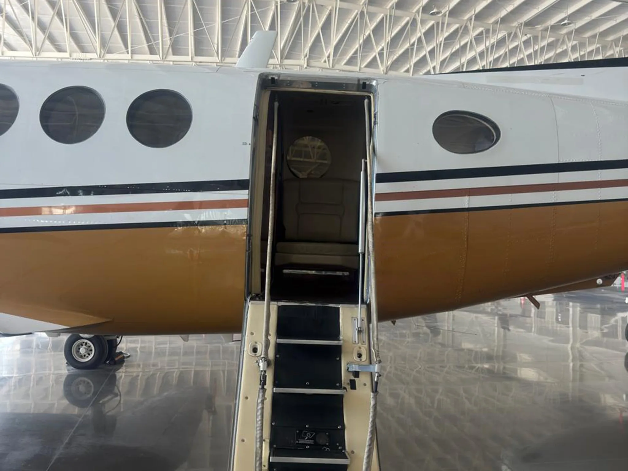 The open airstair door of a white and gold twin-turboprop aircraft, showing steps leading into the cabin.