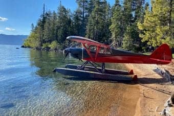 A red and black float plane is beached on a sandy shore.