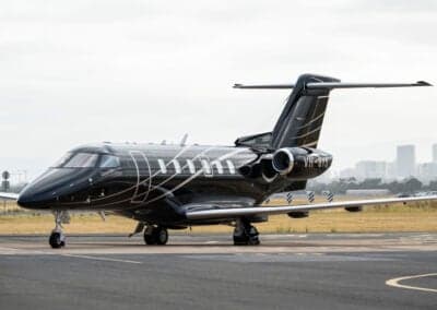 A Pilatus PC-24 jet with a black paint scheme and decorative lines parked on the tarmac.