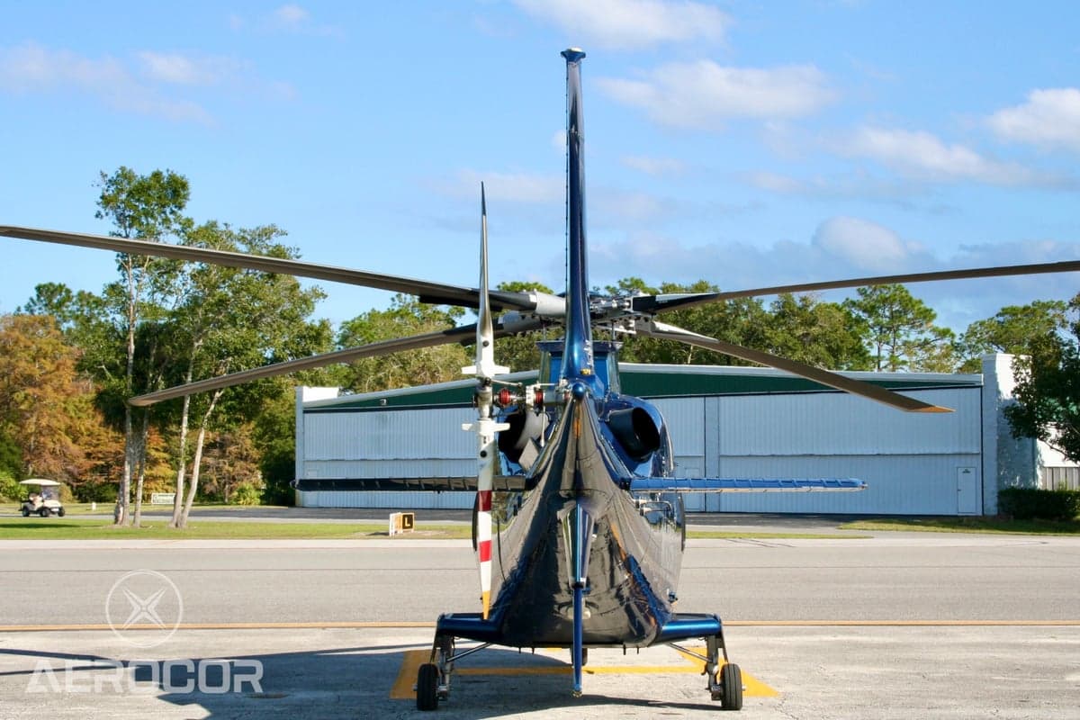 Rear view of a blue AgustaWestland AW109 helicopter (N109TG) parked on an airfield with a hangar in the background.