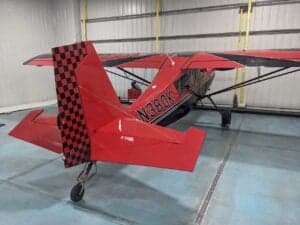 A red and black Cubcrafters aircraft with tail number N380K is parked inside a hangar.