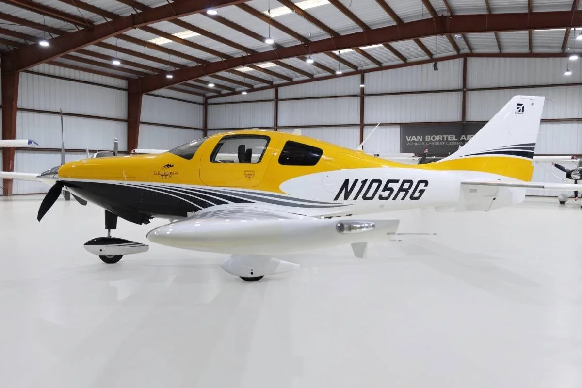 A yellow and white Cessna TTx (N105RG) with black accents, parked in a hangar, viewed from the front-right side.