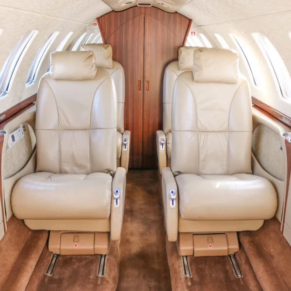 Interior view of an aircraft cabin with two rows of beige leather seats facing each other.