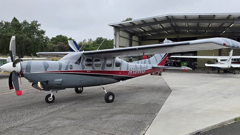 N19WB Cessna Caravan parked on the tarmac in front of a hangar, showing the gray and white striped paint scheme.