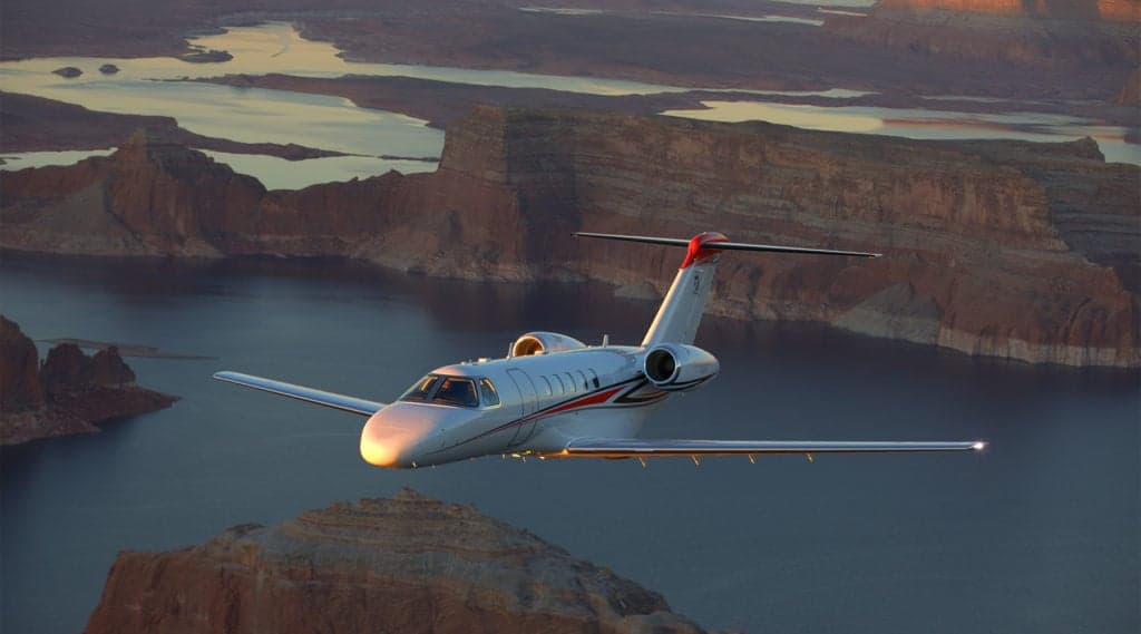A Citation CJ4 flying over a lake and canyon landscape.