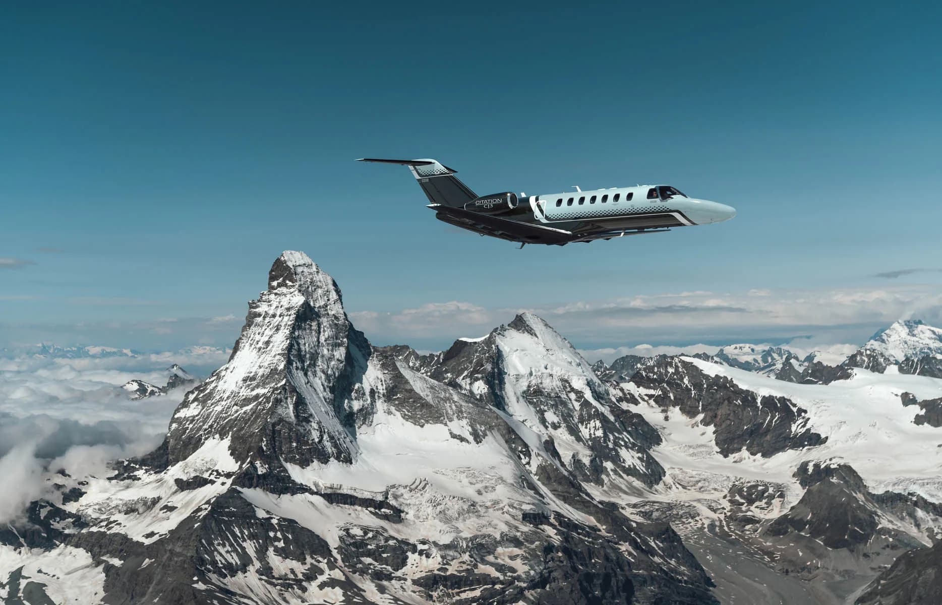 A Citation CJ3 flying over snow-capped mountains.